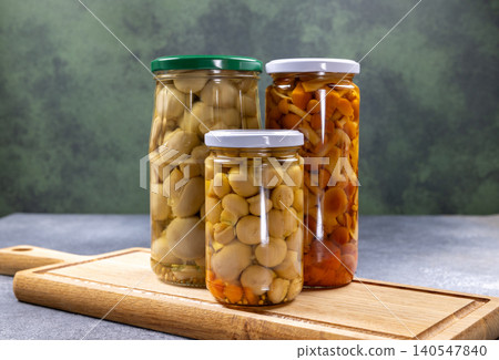 Preserving pickled forest mushrooms in glass jars on chopping board Preserving pickled forest mushrooms in glass jars on chopping board 140547840