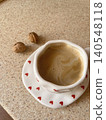 Delightful Cup of Coffee with Heart-Shaped Saucer and Walnuts on a Cozy Surface. 140548118
