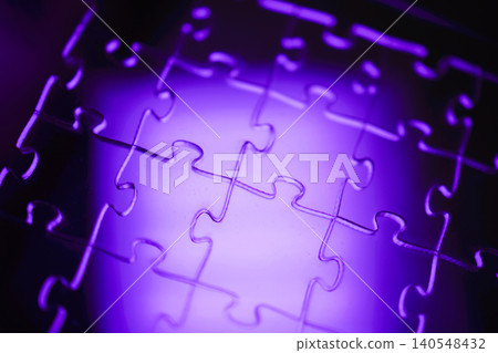 Close-up view of interlocking puzzle pieces illuminated with purple light, showcasing the unique shapes and contours of each piece against a soft background Close-up view of interlocking puzzle pieces illuminated with purple light, showcasing the unique shapes and contours of each piece against a soft background 140548432