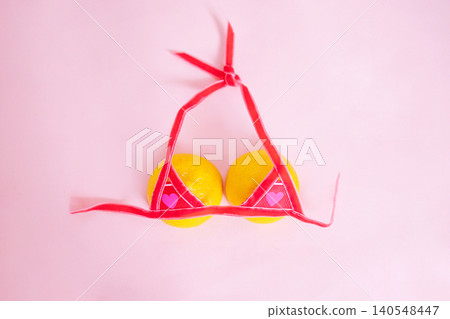 Yellow lemons adorned with a pink bikini top on a soft pink background, creating a playful and whimsical fruit arrangement for summer-themed visuals Yellow lemons adorned with a pink bikini top on a soft pink background, creating a playful and whimsical fruit arrangement for summer-themed visuals 140548447