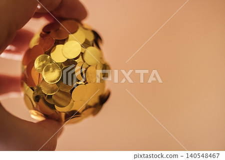Hand holding a decorative golden egg covered in shiny sequins against a soft pastel background, ideal for festive celebrations and holiday decorations Hand holding a decorative golden egg covered in shiny sequins against a soft pastel background, ideal for festive celebrations and holiday decorations 140548467