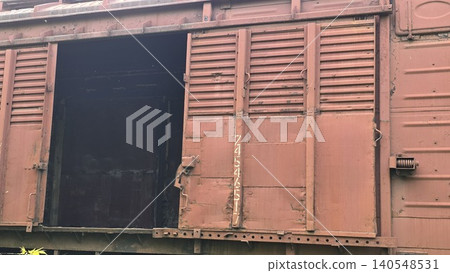 Open sliding door of old rusty red metal freight train car revealing dark empty interior, concept of abandoned railway transport and industrial decay 140548531