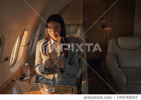 Young Caucasian woman smiling while using a smartphone inside a private jet cabin Young Caucasian woman smiling while using a smartphone inside a private jet cabin 140548685