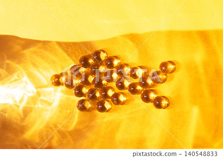 Group of amber-colored gel capsules arranged in an arrow shape on a bright yellow background, showcasing transparency and reflections of light Group of amber-colored gel capsules arranged in an arrow shape on a bright yellow background, showcasing transparency and reflections of light 140548833