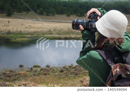A woman photographs Kagami Pond in Ikenotaira Marshland, Tomi City, Nagano Prefecture. A woman photographs Kagami Pond in Ikenotaira Marshland, Tomi City, Nagano Prefecture. 140549094