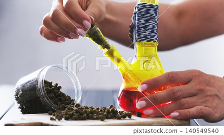 Girl Filling Smoking Bong With Dry CBD Cannabis Girl Filling Smoking Bong With Dry CBD Cannabis 140549540