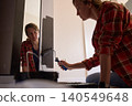 Woman applies dark paint to wall with roller beside mirror, with her reflection visible 140549648