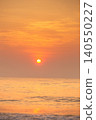 Golden sunset over the ocean with gentle waves and hazy sky 140550227