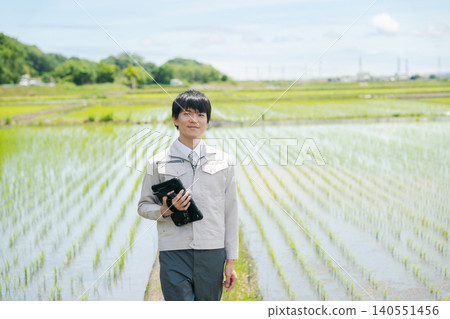 A man in work clothes standing in a rice field. A man in work clothes standing in a rice field. 140551456