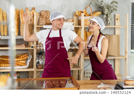 Pair of young bakers in aprons joyfully dancing in bakery Pair of young bakers in aprons joyfully dancing in bakery 140552124