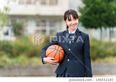 High school, junior high school, and elementary school girls in uniform standing in a schoolyard holding a basketball High school, junior high school, and elementary school girls in uniform standing in a schoolyard holding a basketball 140552185