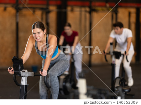 Focused girl works out with exercise bicycle during class at fitness club Focused girl works out with exercise bicycle during class at fitness club 140552309