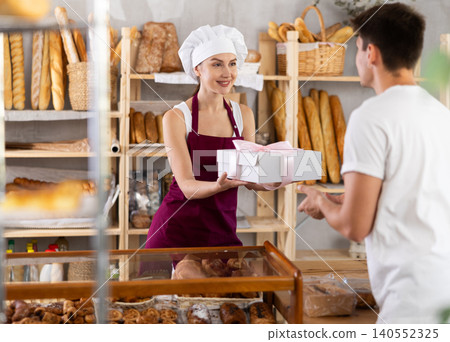 Saleswoman giving cake in white box to male buyer in bakery Saleswoman giving cake in white box to male buyer in bakery 140552325