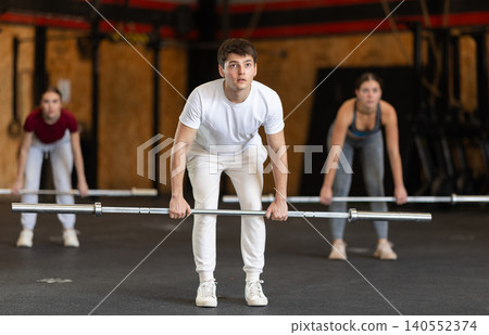 Slender guy trains muscles of arms and back using barbell and differentiated weighting in gym Slender guy trains muscles of arms and back using barbell and differentiated weighting in gym 140552374