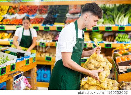 Concentrated male seller stacking up mesh bag with potatoes in shop Concentrated male seller stacking up mesh bag with potatoes in shop 140552662