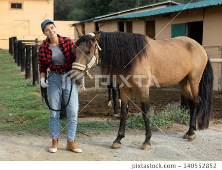 Portrait of female owner of horse farm shows her farm against backdrop of corral for walking horses Portrait of female owner of horse farm shows her farm against backdrop of corral for walking horses 140552852