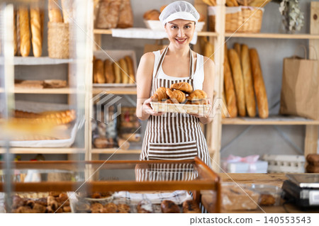 Young saleswoman displays croissants in square wicker basket Young saleswoman displays croissants in square wicker basket 140553543