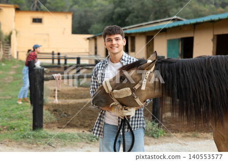 Portrait of young man of horse farm shows farm against the backdrop of corral for walking horses 140553577