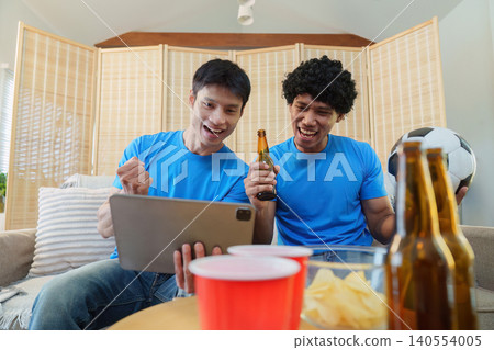 Asian men celebrating soccer game victory on tablet at home Asian men celebrating soccer game victory on tablet at home 140554005