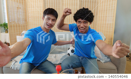 Asian men celebrating soccer game victory with excitement at home Asian men celebrating soccer game victory with excitement at home 140554046