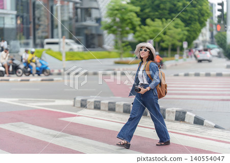 Asian woman tourist walking on urban crosswalk with camera for city exploration and summer travel 140554047