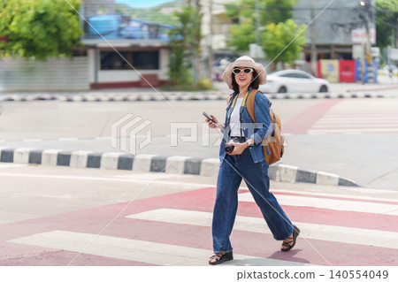 Happy Asian woman tourist walking on crosswalk with camera and phone for urban travel adventure Happy Asian woman tourist walking on crosswalk with camera and phone for urban travel adventure 140554049