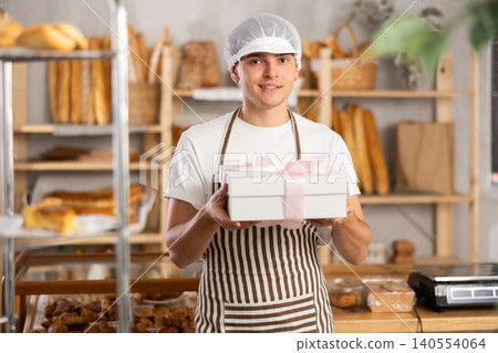 Smiling young salesman presenting gift box with cake in bakery Smiling young salesman presenting gift box with cake in bakery 140554064