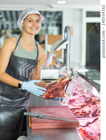 Positive young saleswoman demonstrating piece of meat in butcher shop Positive young saleswoman demonstrating piece of meat in butcher shop 140554162