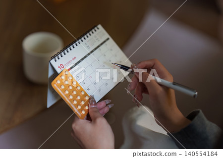 Woman marking calendar with birth control pills for health planning Woman marking calendar with birth control pills for health planning 140554184