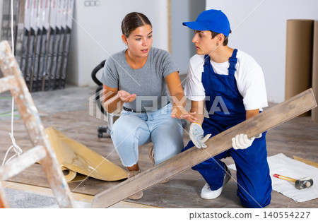Young woman talking to builder during laminate flooring installation in apartment Young woman talking to builder during laminate flooring installation in apartment 140554227