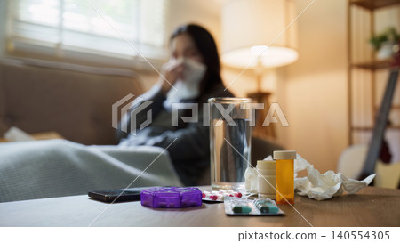 Sick Asian woman resting on couch with medication on table Sick Asian woman resting on couch with medication on table 140554305