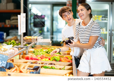 Young woman and young guy choose eggplants in grocery store Young woman and young guy choose eggplants in grocery store 140554452