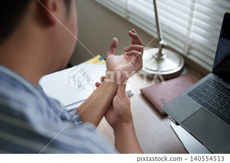 Asian man experiencing wrist pain while working at home office 140554513