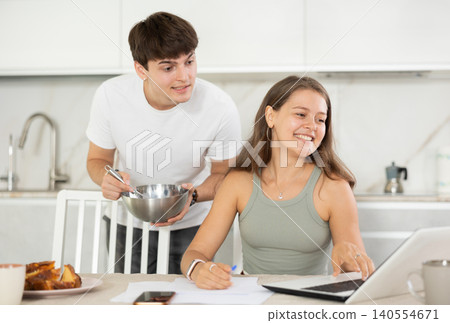 Happy young woman using laptop in the kitchen while communicating with her boyfriend Happy young woman using laptop in the kitchen while communicating with her boyfriend 140554671