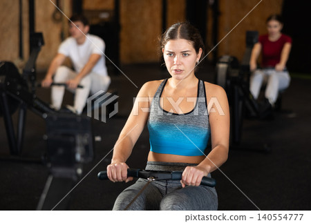 Focused girl works out with rowing machine during class at fitness club Focused girl works out with rowing machine during class at fitness club 140554777