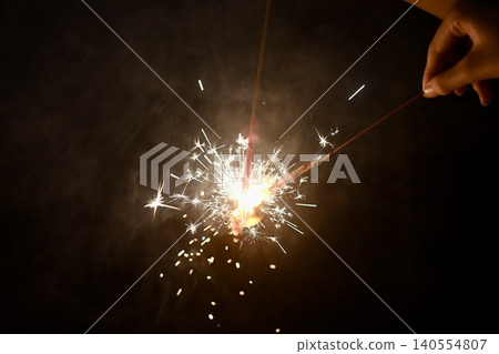 Handheld fireworks glow in the darkness of night, creating a magical display of sparks and smoke. 140554807