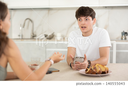 Happy young couple sitting at the kitchen-table and having conversation while drinking tea 140555043