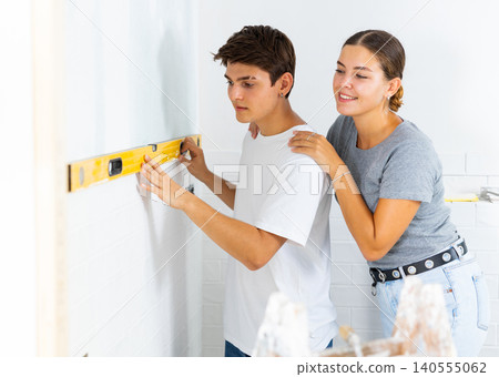 Young couple uses a spirit level on the wall Young couple uses a spirit level on the wall 140555062