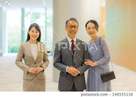 Staff member guiding a middle-aged couple to the event hall. Staff member guiding a middle-aged couple to the event hall. 140555138