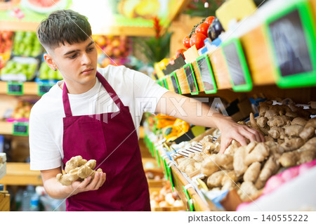 Young salesman working in store lays out ginger roots on counter 140555222