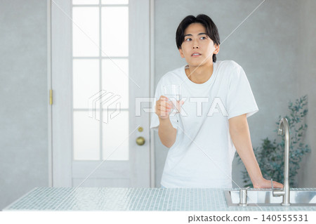 一名男子正在用玻璃杯喝水。 一名男子正在用玻璃杯喝水。 140555531