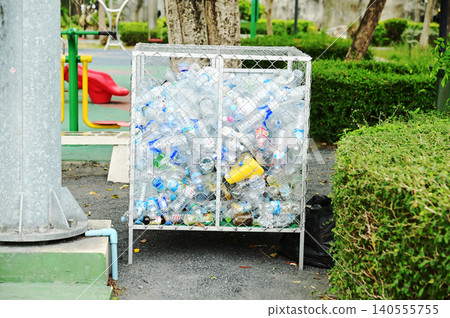 Disposable plastic water bottles are collected in a wire mesh bin located in a public park. 140555755