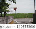 A stop sign stands on the riverbank, a rural Japanese road with a clear blue sky and lush greenery. 140555930