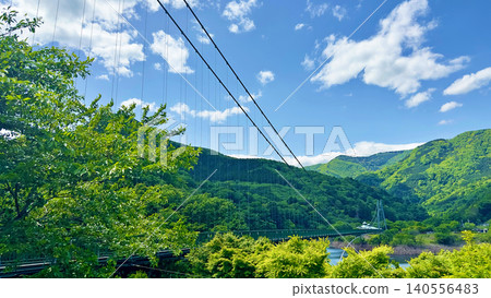 A beautiful, large suspension bridge spanning a valley surrounded by a refreshing blue sky and lush green mountains. A beautiful, large suspension bridge spanning a valley surrounded by a refreshing blue sky and lush green mountains. 140556483