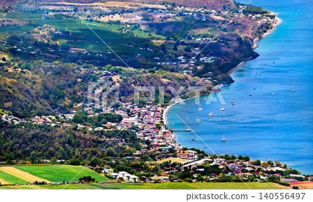 Aerial view of Saint Pierre town and bay in Martinique, featuring lush mountains, a coastal village, and boats in the blue Caribbean Sea. Aerial view of Saint Pierre town and bay in Martinique, featuring lush mountains, a coastal village, and boats in the blue Caribbean Sea. 140556497