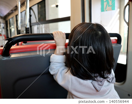 A young girl's back view as she sits in the back seat of a bus and looks at the scenery | Web, publishing, parenting, public transport, local PR 140556944