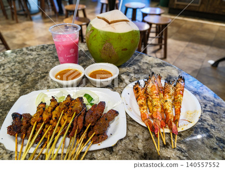 Delicious Singaporean street food featuring grilled chicken and beef satay skewers with fresh coconut and local drinks at a hawker center Delicious Singaporean street food featuring grilled chicken and beef satay skewers with fresh coconut and local drinks at a hawker center 140557552