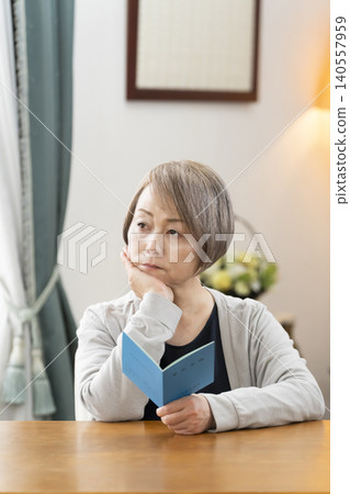 A senior woman looking at her pension book in the living room A senior woman looking at her pension book in the living room 140557959