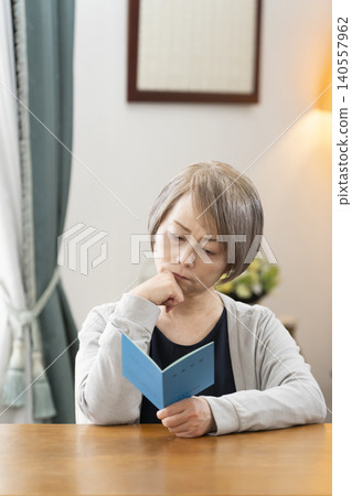 A senior woman looking at her pension book in the living room A senior woman looking at her pension book in the living room 140557962