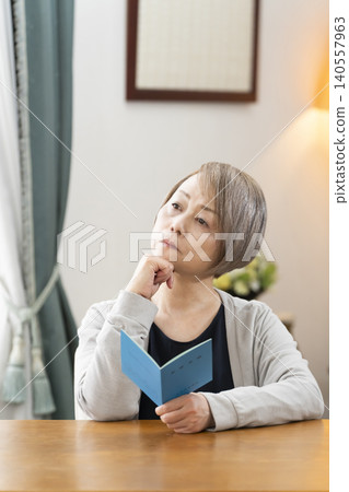 一位老婦人在客廳看著她的退休金手冊。 140557963